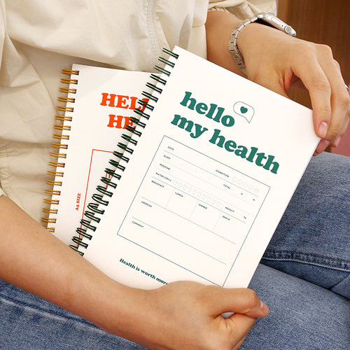 One journal has an orange “HELLO MY HEALTH” title, and the other has a green “hello my health” title with a health tracking form visible on the cover. hold by a woman wearing a jean trouser 